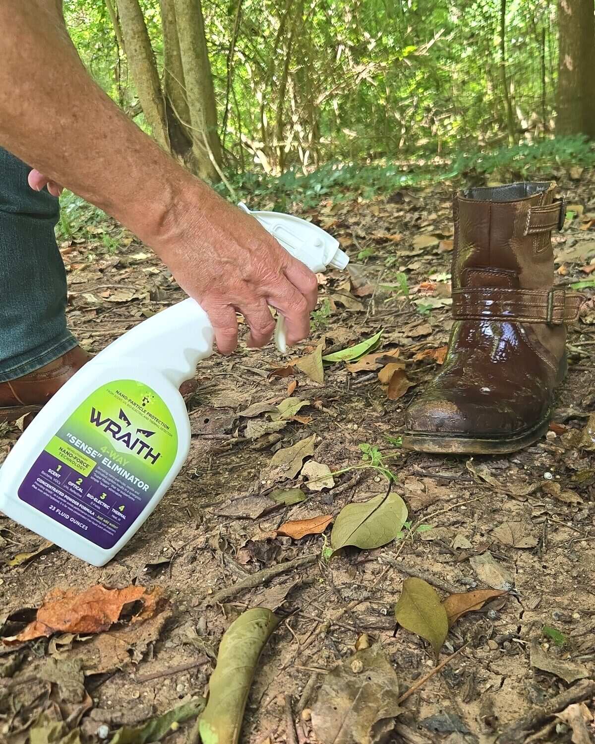 A hand spraying WRAITH from the 23 oz bottle onto a leather hunting boot in the leaf litter
