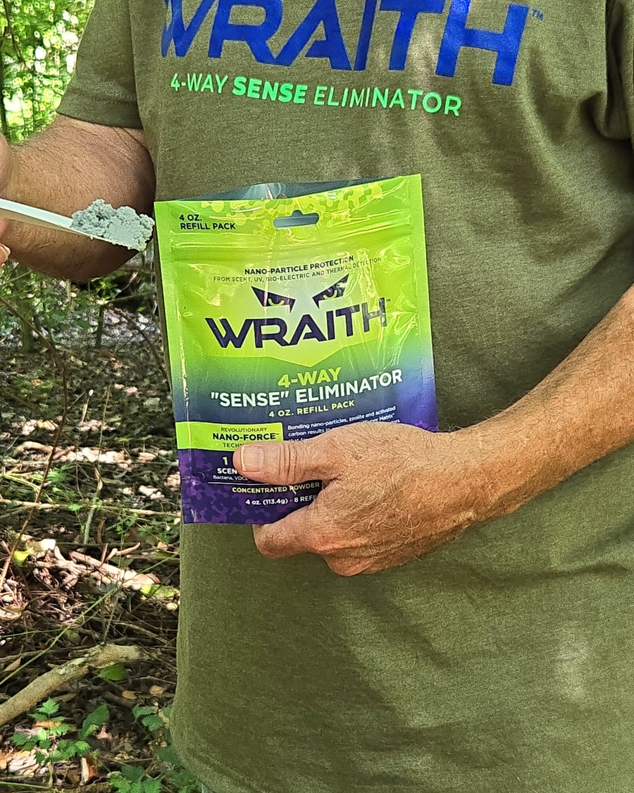 In the field: a hunter in a WRAITH t-shirt holding the 4 oz refill pouch in green timber