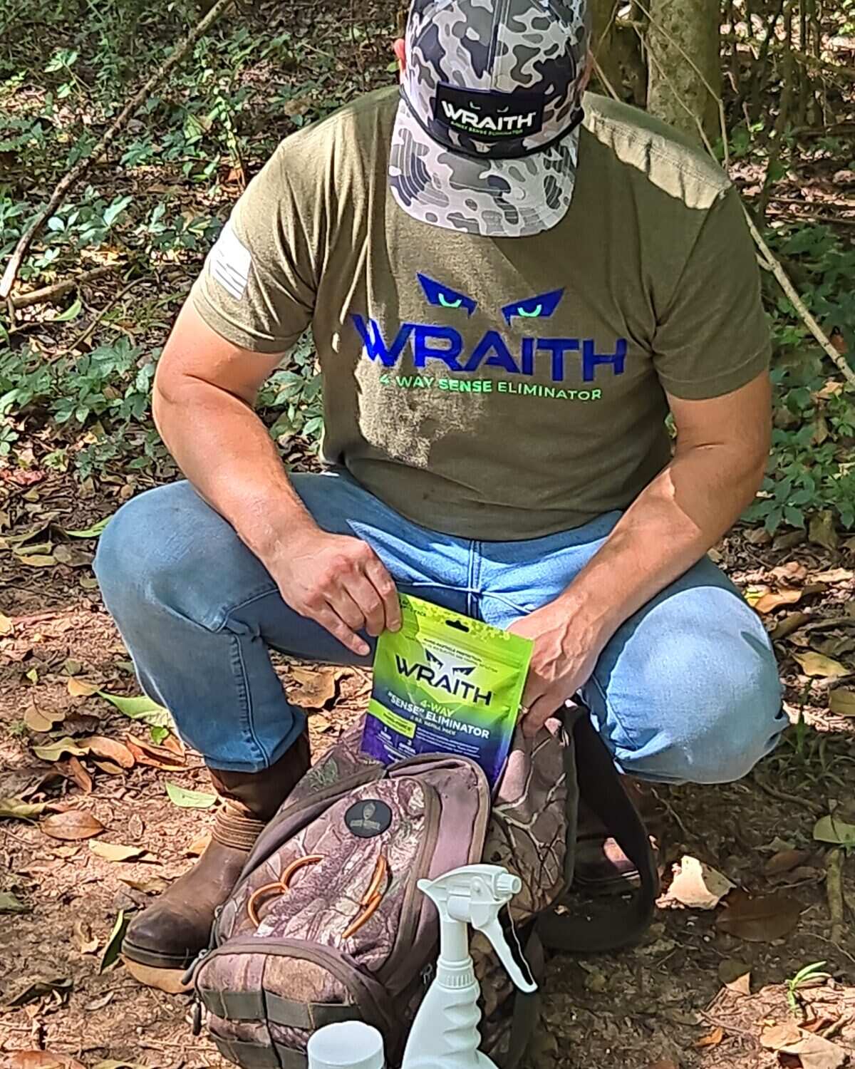 A hunter crouched over a hunting pack, holding the 4 oz WRAITH refill pouch, spray bottle on the ground beside him