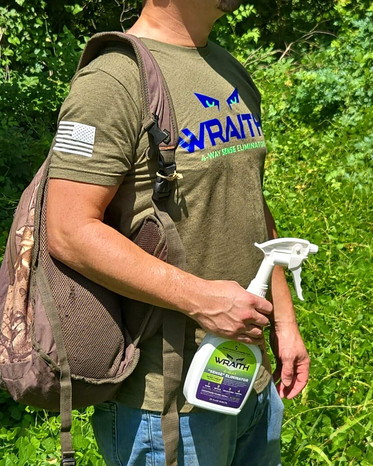 A hunter walking out through green timber with a pack over one shoulder and the WRAITH spray bottle in hand